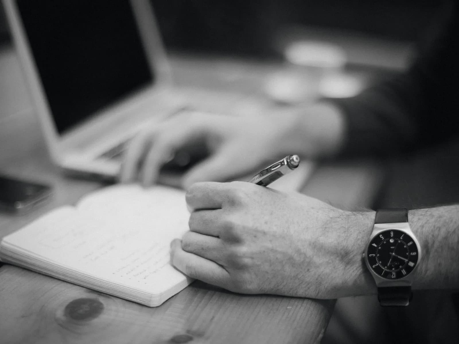 Hands writing notes beside a laptop