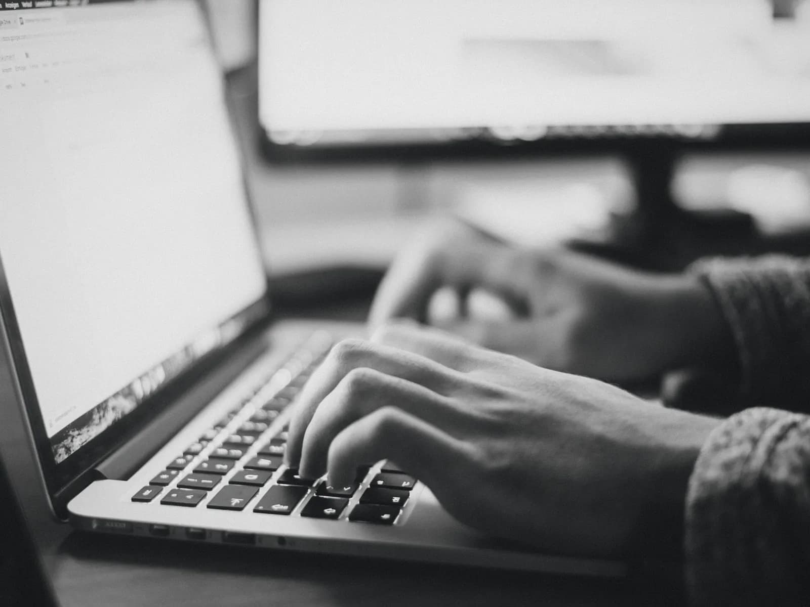 Hands typing at a laptop with charts on the screen behind